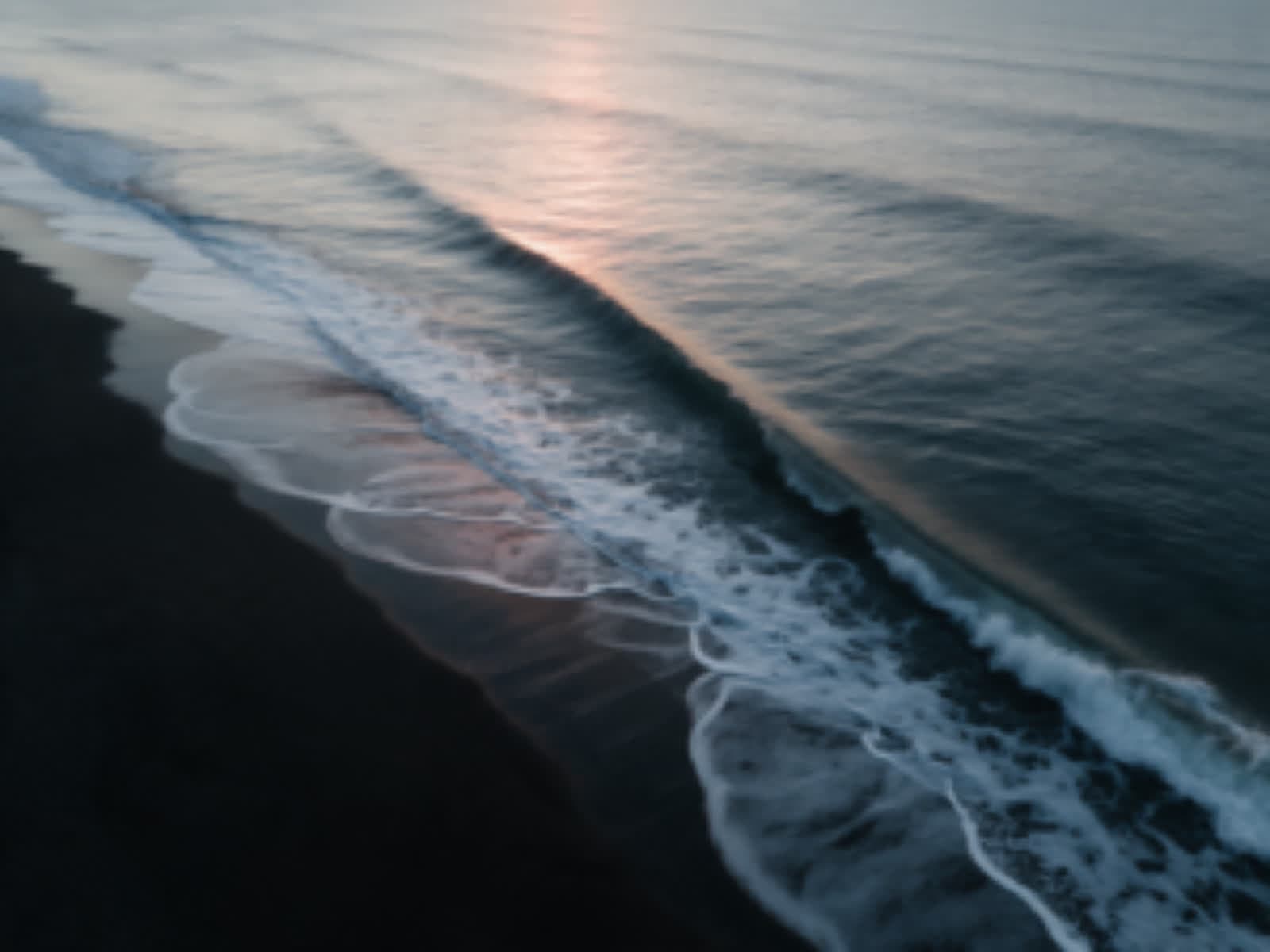Soft, low resolution aerial frame of a wave on black sand